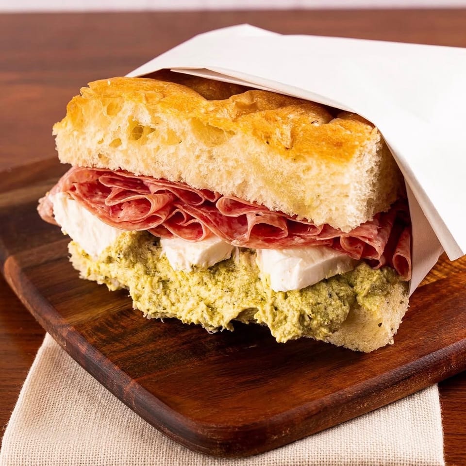 Focaccia sandwich with salami, mozzarella, and pesto on a wooden board.